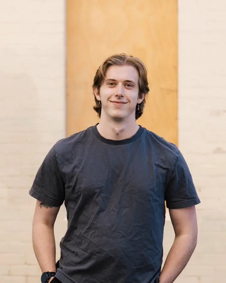 Connor Geldard, smiling, standing in front of a pale brick wall